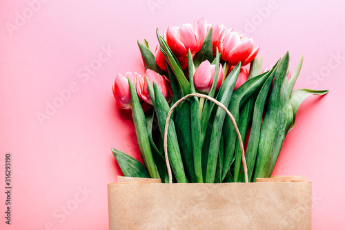 Beautiful tulips bouquet in bag on pink background