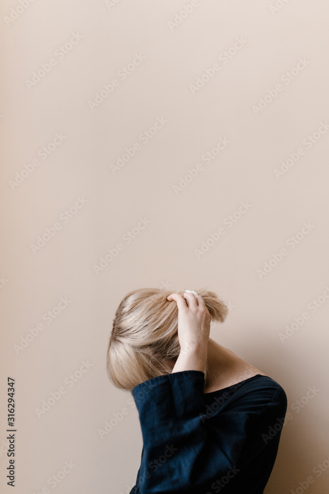 Woman with blonde hair standing in front of a neutral wall Woman with blonde hair standing in front of a neutral wall