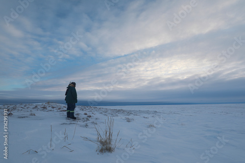 Man in winter clothing standing on snow watching the weather on tundra landscape while holding a rifle, near Arviat, Nunavut, Canada photo