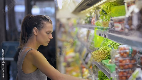 woman choosing lettuce in organic vegetables department refrigerator. female customer buying heathy vegetarian fresh green food. fridge in grocery store. concept shopping