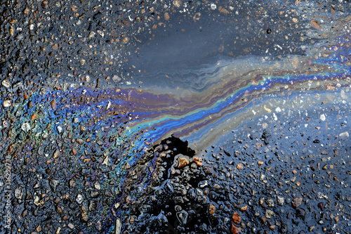Iridescent oil sheen abstract. Oil stains are mobilized after rainstorm and form streaks on pavement 