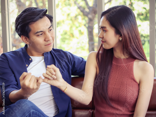 attractive couple sitting on couch in living room. a man and his girlfriend hands reconcile with clasping each other's little finger.Selective focus on man's face