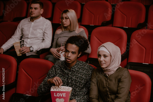 Multiethnic friends with popcorn watching movie in cinema photo