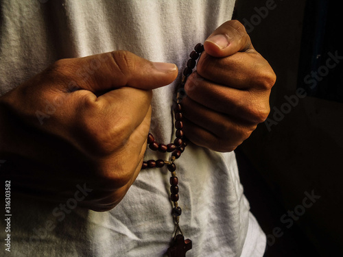 Photography Young Afro Brazilian woman holding with both hands a rosary with the cross of Jesus Christ