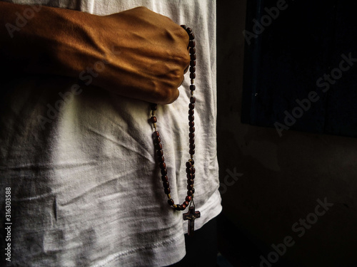 Young Afro Brazilian woman holding with both hands a rosary with the cross of Jesus Christ.