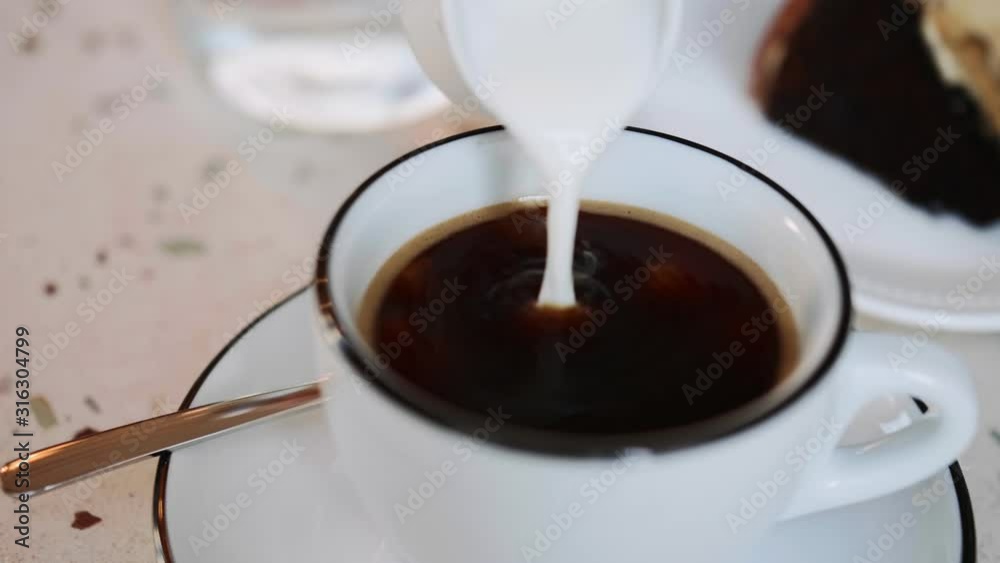 Pouring milk in coffe in cafe