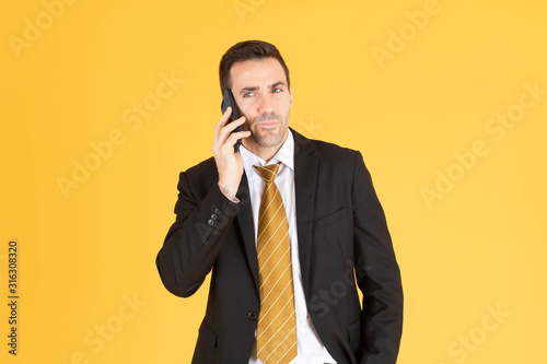 Portrait of confident businessman using smartphone on yellow background.