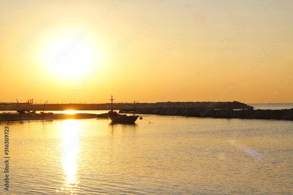 The sun rises in the morning along the coast, with boats mooring around the dam preventing coastal erosion.