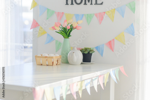 Принти на полотні Easter home decorations, multi-colored flags, tulips and eggs on a white table o