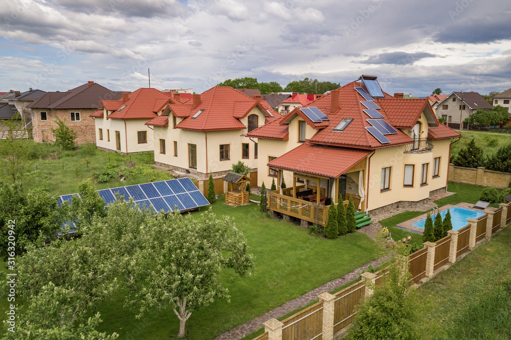 Aerial view of a new autonomous house with solar panels and water heating radiators on the roof and green yard with blue swimming pool.