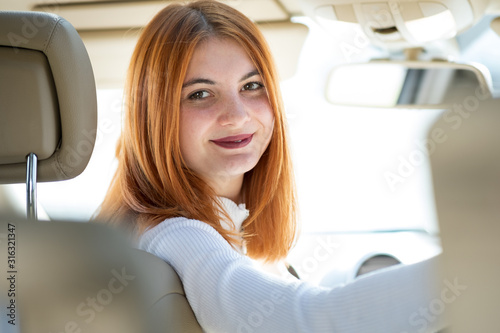 Young redhead woman driver driving a car smiling happily.