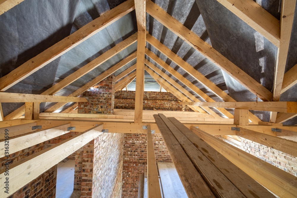 Obraz premium Attic of a building under construction with wooden beams of a roof structure and brick walls.