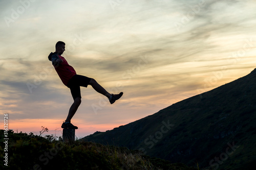 Wallpaper Mural Dark silhouette of a hiker balancing on a summit stone in evening mountains. Torontodigital.ca
