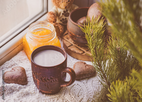 Handmade coffee with milk in a clay mug, heart-shaped cookies and orange jam, breakfast on the windowsill
