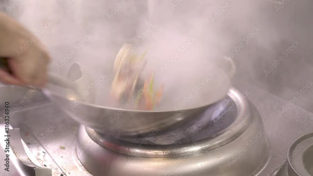 Close up handheld shot of chef hands cooking slices of vegetables in frying pan. Close up of cooking vegetables in chinese frying pan in asian kitchen restaurant Close up handheld shot of chef hands cooking slices of vegetables in frying pan. Close up of cooking vegetables in chinese frying pan in asian kitchen restaurant