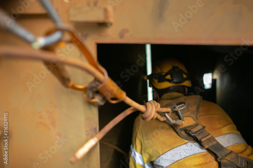 Close up shot of rope access worker wearing safety harness, helmet connecting three two one rescue pulley system into back of his safety harness  loop prior entering working inside confined space  