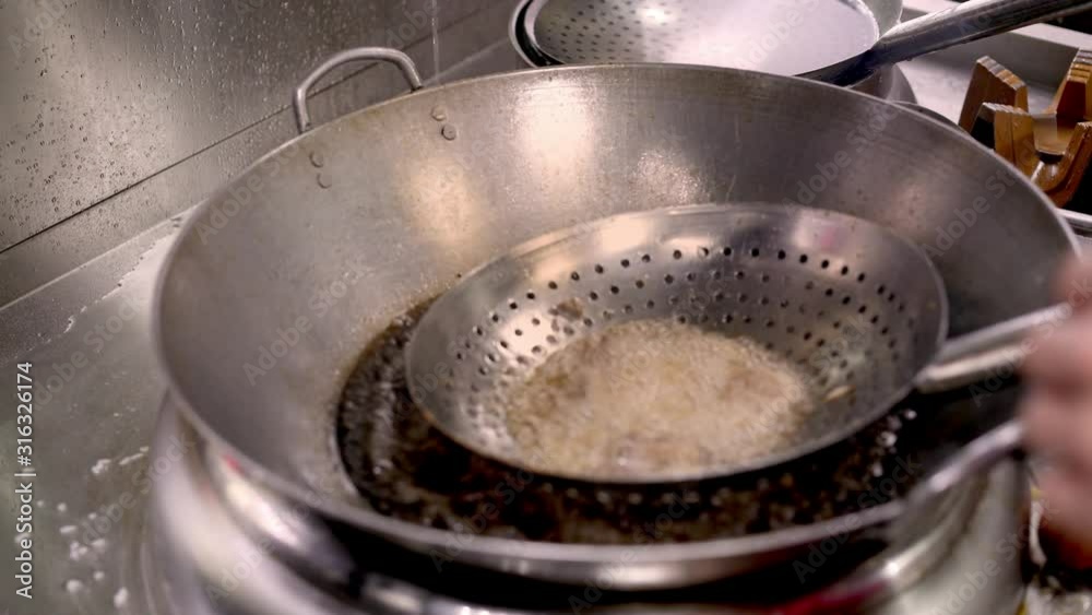 Close up handheld shot of chef hands frying pieces of meat on a spoon with holes in boiling oil. Cooking frying meat in asian kitchen restaurant Close up handheld shot of chef hands frying pieces of meat on a spoon with holes in boiling oil. Cooking frying meat in asian kitchen restaurant