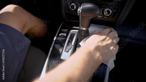driver is wiping panel of gear box in automobile, holding wet napkin in hand, closeup view inside car