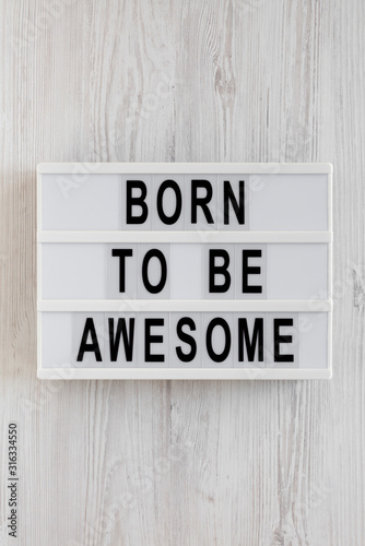 'Born to be awesome' words on a modern board on a white wooden background, top view. Overhead, from above, flat lay. Close-up.