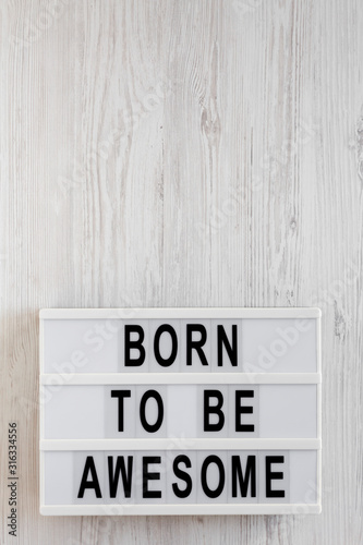 'Born to be awesome' words on a lightbox on a white wooden background, top view. Overhead, from above, flat lay. Copy space.