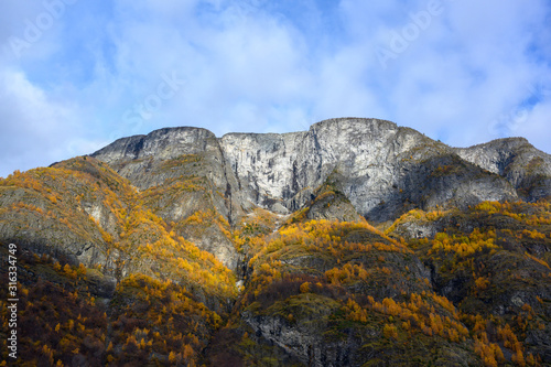 The large rocky mountains on the top of the mountain are snow white and blue sky with clouds and the leaves turning yellow in autumn season.