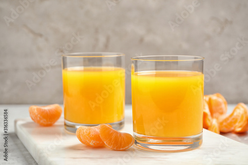 Glasses of fresh tangerine juice and fruits on light table