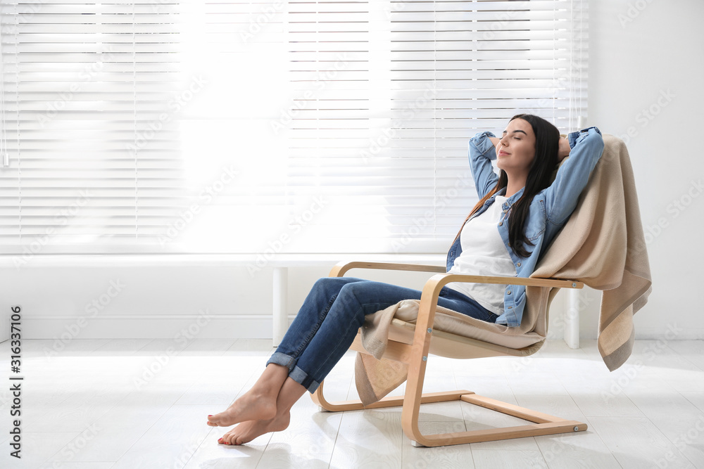 Young woman relaxing in armchair near window at home - obrazy, fototapety, plakaty 