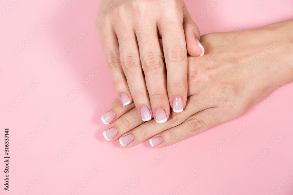 Top view flatlay closeup photography of two female hands with beautiful classic french pink and white manicure. Fingers isolated on pastel pink background. Horizontal color image.