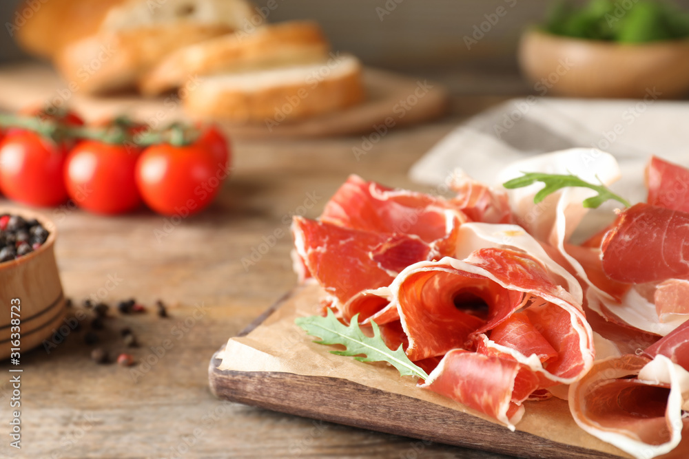Pile of tasty prosciutto on wooden table, closeup