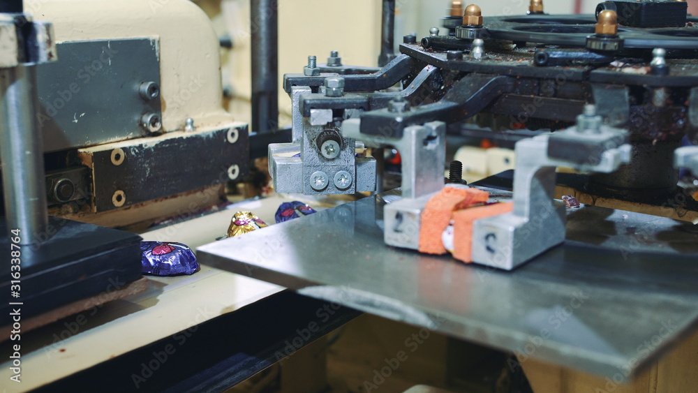 Fototapeta premium Candy factory. Industrial machine wrapping candies. Modern industrial machine wrapping tasty sweets and putting them on conveyor on confectionery factory.