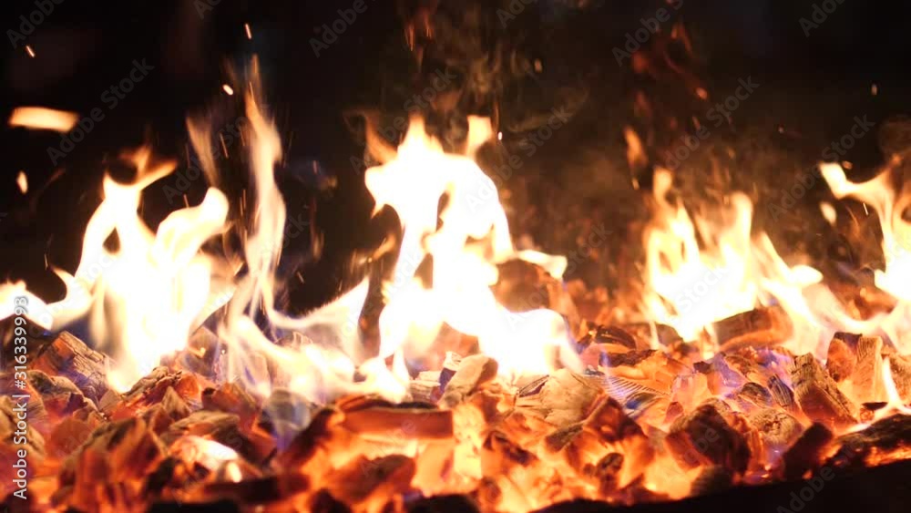 Hot fire smolder wooden coals embers burning in fireplace bright red and yellow colors on dark background in slow motion Hot fire smolder wooden coals embers burning in fireplace bright red and yellow colors on dark background in slow motion