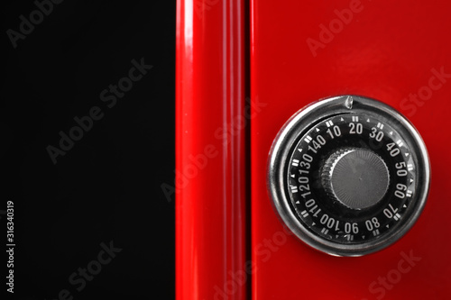 Red steel safe with mechanical combination lock on black background, closeup