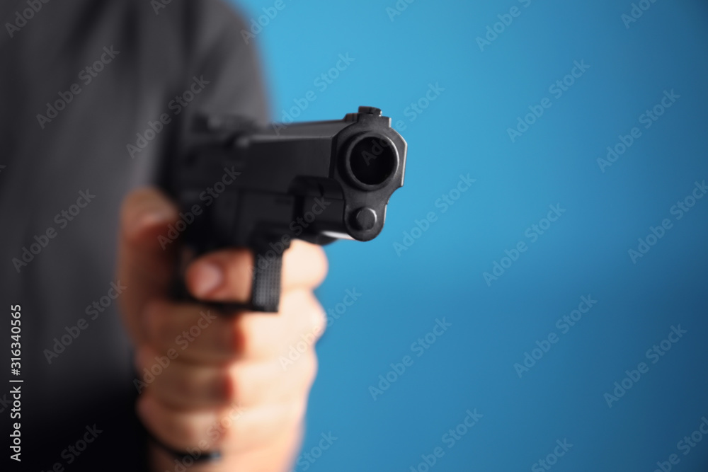 Man holding gun on blue background, closeup Man holding gun on blue background, closeup