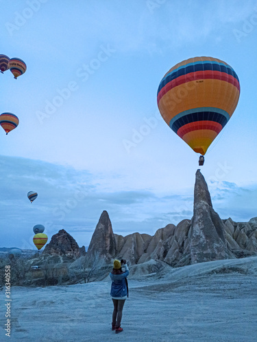 Young woman watching Colorful Hot Air Balloons at early morning with rocky landscape in Cappadocia, Turkey
