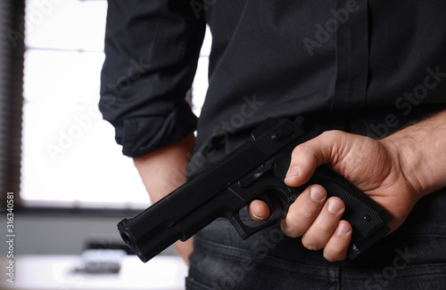 Man holding gun indoors, closeup. Dangerous criminal