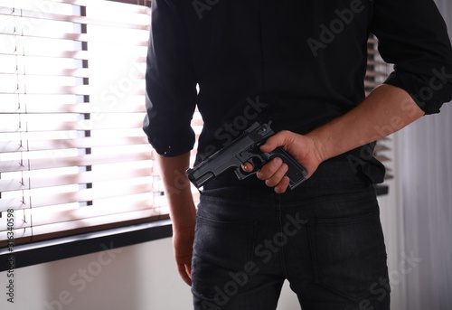 Man with gun near window indoors, closeup
