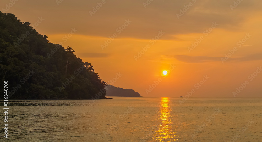sea view evening of rocks cape in the sea with yellow sun in orange sky background, sunset at Khao Chong Kad, Surin island, Mu Ko Surin National Park, Phang Nga, southern of Thailand.