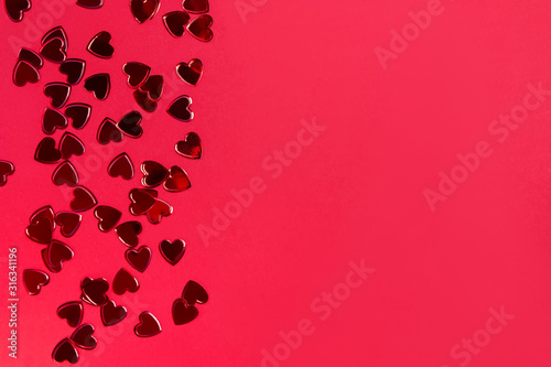 Small red heart shaped confetti on red background