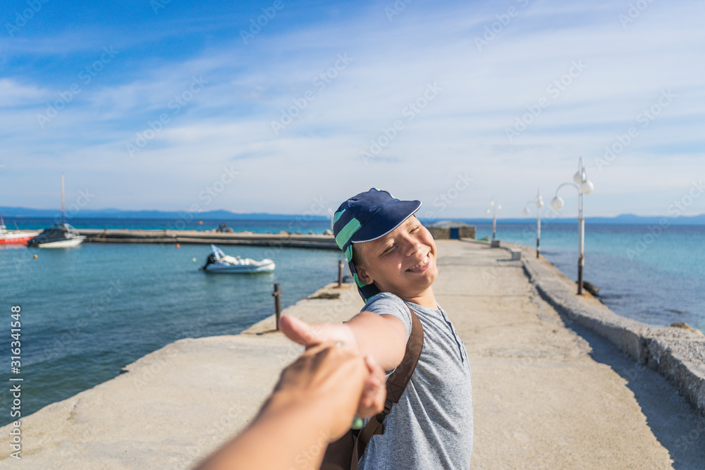 Point of view photography of mother and son holding hands togeter while walking on sunny summer beach during holidays in Greece. Love and happiness concept. Woman and boy holding hands. 