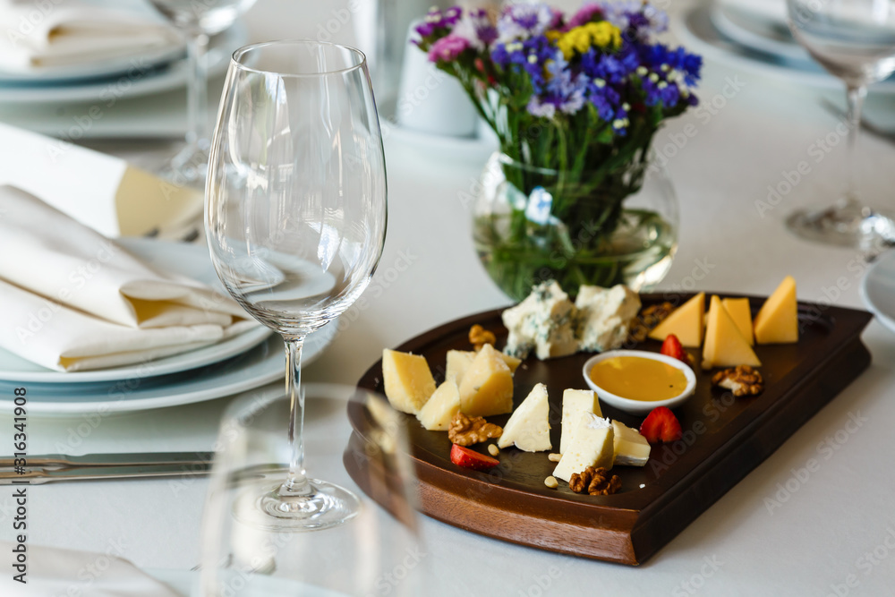 Wine and cheese concept, cheeseboard in a restaurant, variety of cheese and sauce, empty wineglass. Cheese tasting, banquet party, celebration