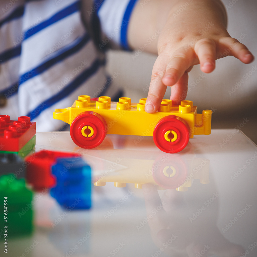 The kid plays with colorful cubes. The child holds in his hand a colored toy with wheels. Early development for children. Home Educational Games The kid plays with colorful cubes. The child holds in his hand a colored toy with wheels. Early development for children. Home Educational Games