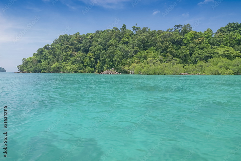 view of blue-green sea with green forest on island with blue sky background, journey to Moken village, Mu Ko Surin National Park, Phang Nga, southern of Thailand.