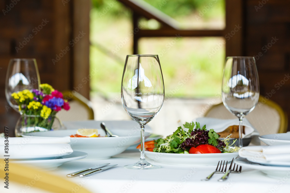 Restaurant table served for two persons. Wine glasses, plates, silverware, cutlery. European food, vegan organic salad. Banquet snacks Restaurant table served for two persons. Wine glasses, plates, silverware, cutlery. European food, vegan organic salad. Banquet snacks