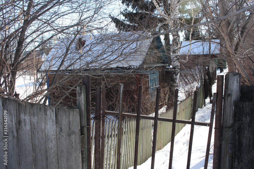 an old wooden house in a Siberian village behind a lattice fence in winter in the snow an old wooden house in a Siberian village behind a lattice fence in winter in the snow