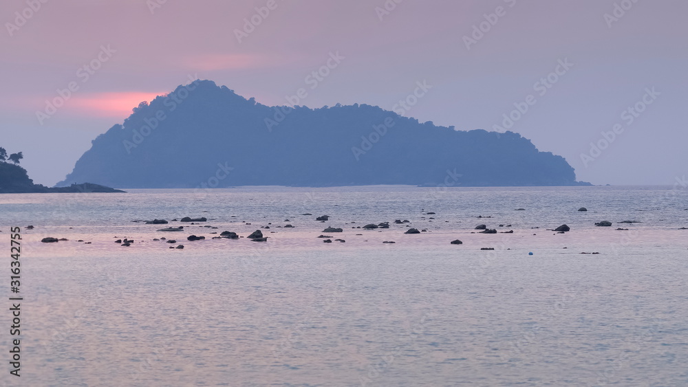 view of many small rocks in the sea with mountain and purple sky in background, sunset at Khao Chong Kad, Surin island, Mu Ko Surin National Park, Phang Nga, southern of Thailand.