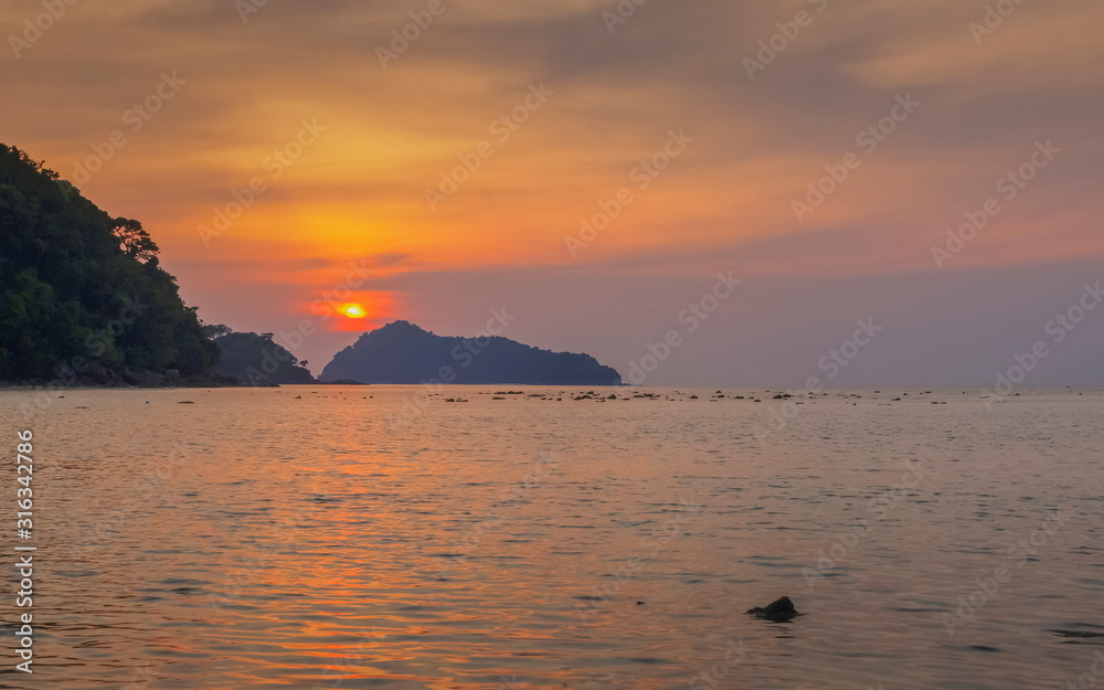 view of mountain in the sea with orange sun light in the sky background, sunset at Khao Chong Kad, Surin island, Mu Ko Surin National Park, Phang Nga, southern of Thailand.