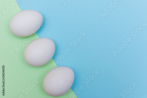 Three Easter holiday flat lay with white egg on a solid light green and blue pastel background with copy space.