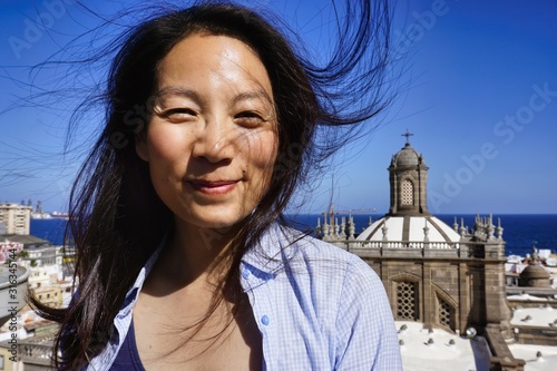 beaming, beautiful young woman on holiday, hair blowing in the wind, in front of a blue summer sky