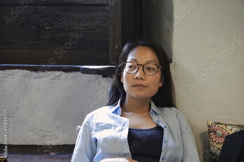 beautiful young woman sitting by a sunny window in a relaxed pose wearing glasses and casual clothes