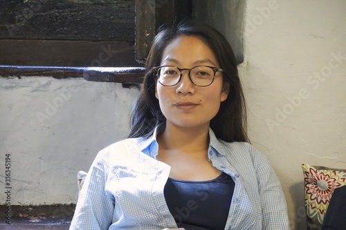 beautiful young woman sitting by a sunny window in a relaxed pose wearing glasses and casual clothes